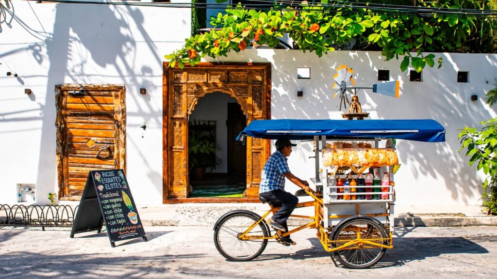 Vendeur ambulant mexicain à vélo avec son chariot de spécialités locales dans une rue ensoleillée de Playa del Carmen, au Mexique.