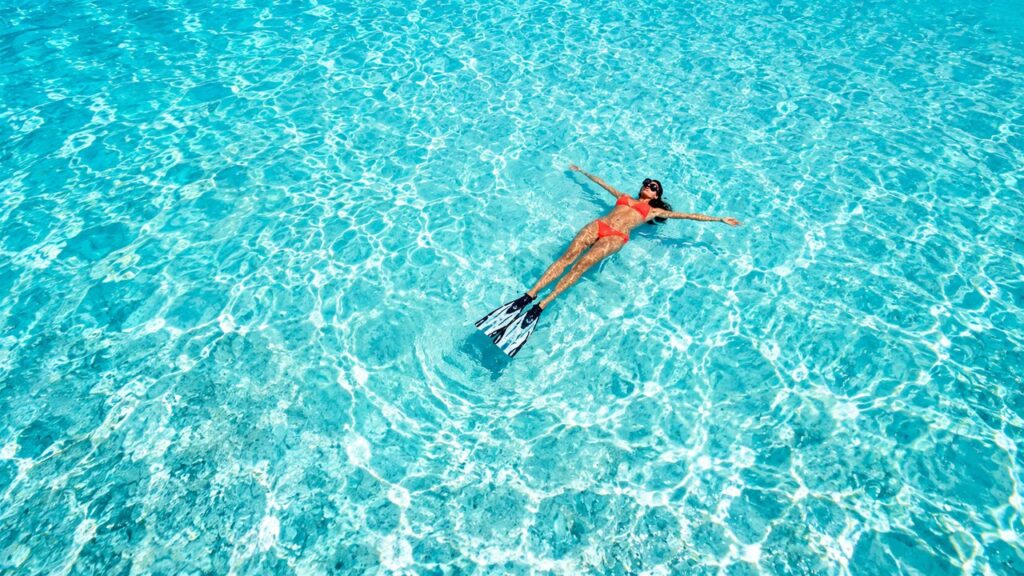 Femme flottant dans une eau turquoise cristalline avec des palmes, vue aérienne d'une baignade dans les Caraïbes au Mexique.
