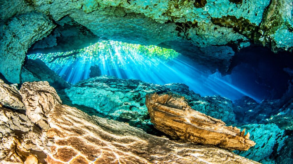 Cénote souterrain du Yucatán au Mexique, avec une eau turquoise cristalline, des formations rocheuses et des rayons de soleil traversant une grotte immergée.
