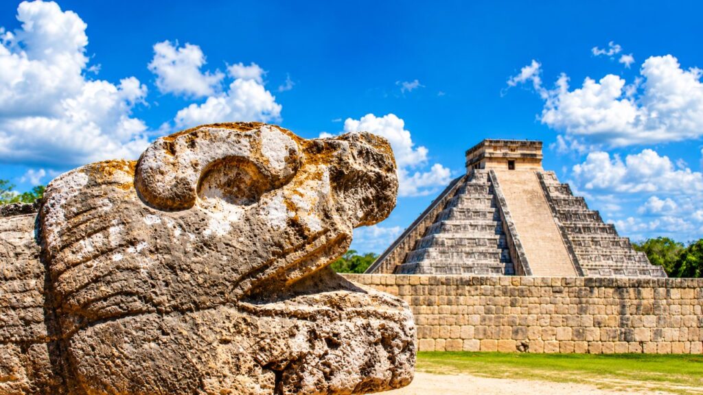 Pyramide de Kukulcán à Chichén Itzá avec une sculpture de serpent maya au premier plan, dans le Yucatán au Mexique.