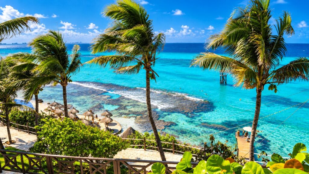 Vue panoramique sur une plage tropicale bordée de palmiers et les eaux turquoise de la mer des Caraïbes au Mexique.