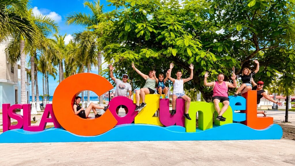 Groupe de touristes francophones devant les lettres colorées de Cozumel lors d'une excursion au Mexique.