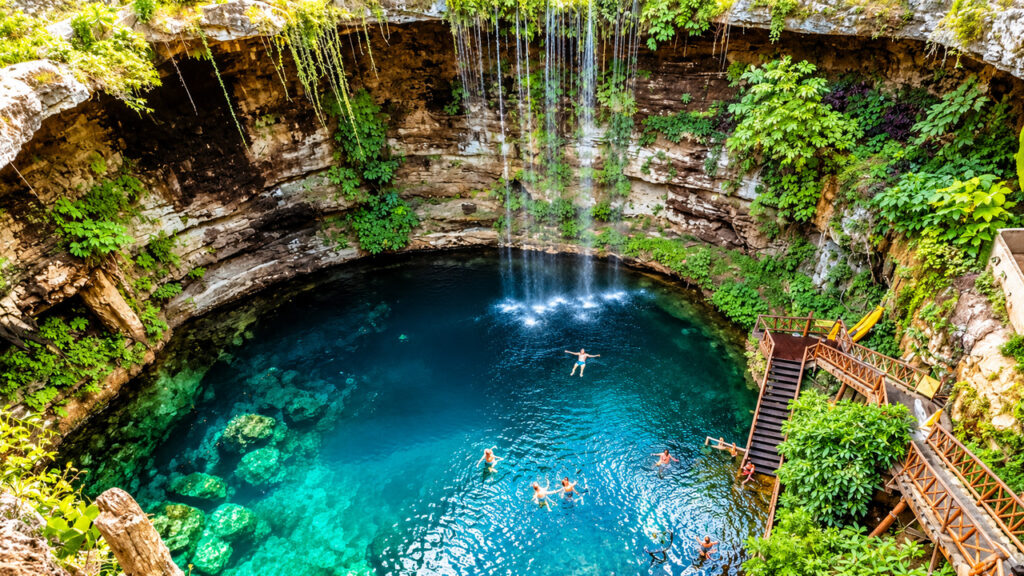 Cénote spectaculaire aux eaux turquoise avec cascade, végétation tropicale et escalier en bois dans la région du Yucatán au Mexique.