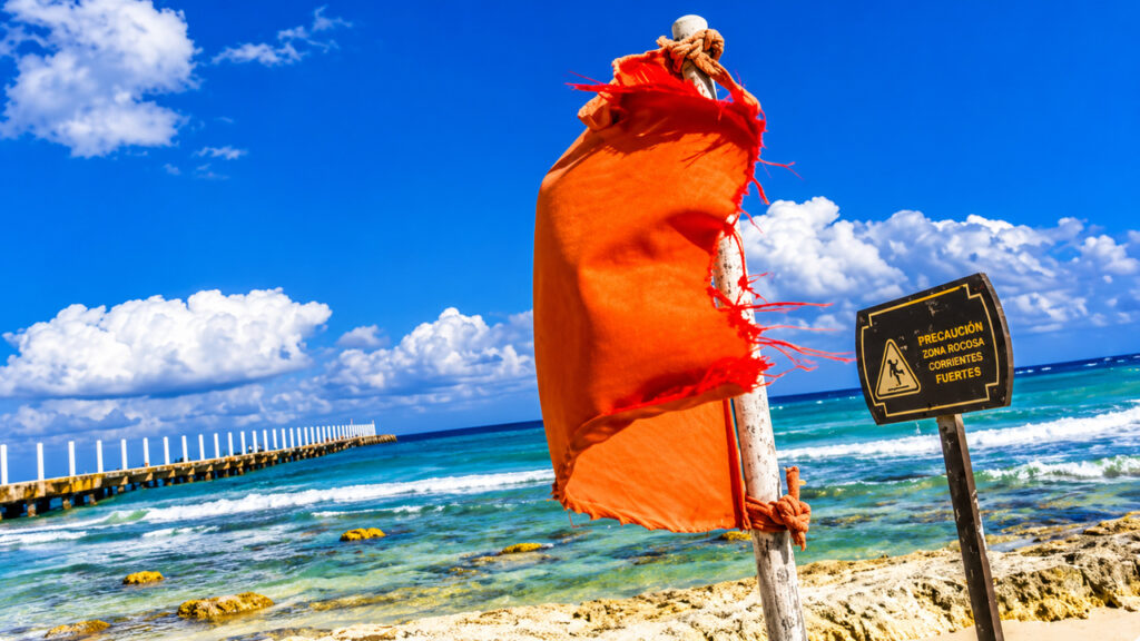 Drapeau orange de sécurité sur une plage de la Riviera Maya au Mexique, signalant des conditions de baignade dangereuses.
